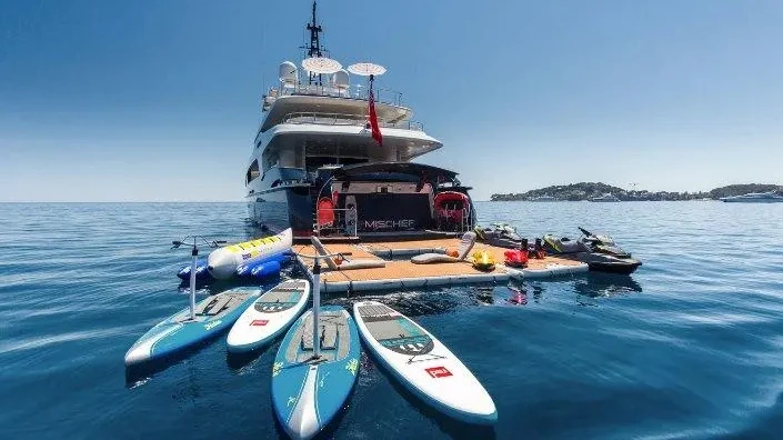 A superyacht surrounded by water toys, paddleboards and jet skis